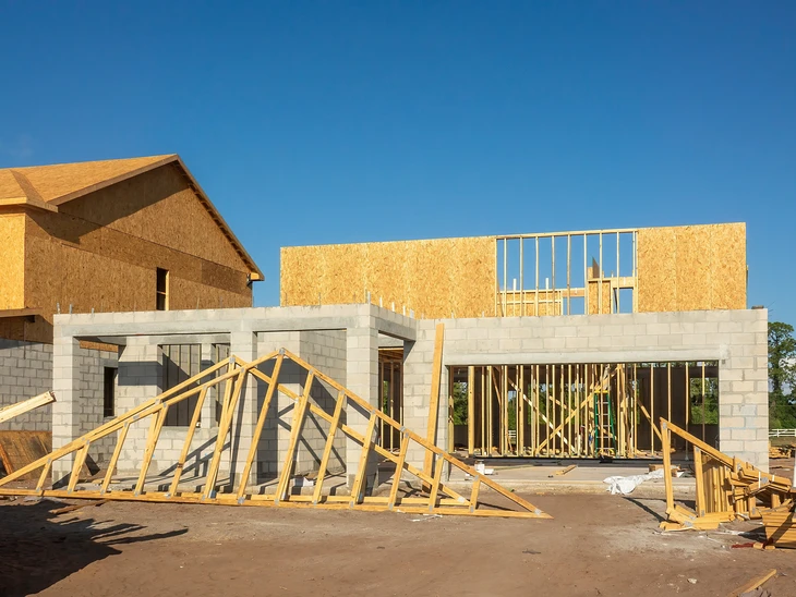 Chantier de construction résidentielle en cours, structure béton préfabriqué partiellement assemblée sous ciel bleu nuageux