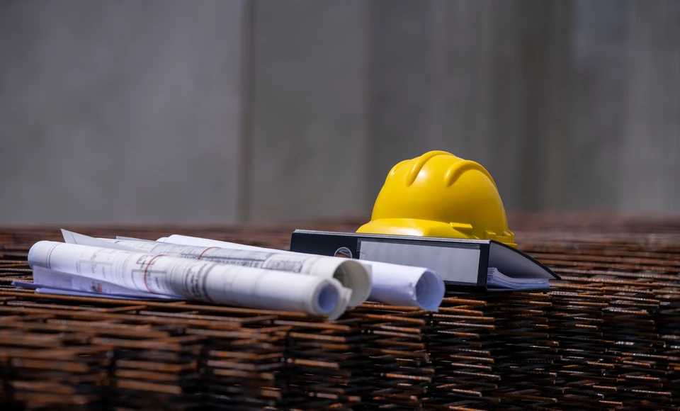 Deux professionnels du bâtiment examinent des plans architecturaux dans un bureau ensoleillé